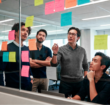 A team of professionals brainstorms together, focused on a glass wall covered in colorful sticky notes during a strategy session.